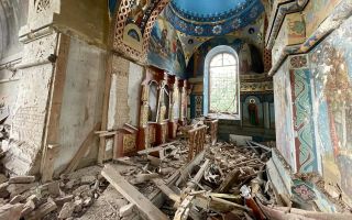 Foto van een verwoest kerkinterieur. Op de achtergrond is een ruimte te zien met een hemelsblauwe koepel en een raam waar licht door naar binnen valt. Links en rechts zijn muurschilderingen te zien. Op de vloer liggen stenen en houten balken door elkaar.