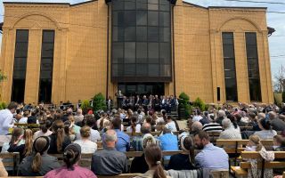 Geel stenen kerkgebouw met daarvoor banken met mensen erop.