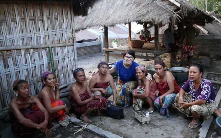 Acht vrouwen zitten gehurkt in een halve cirkel op de grond. In het midden zit een vrouw met een blauw shirt die de armen om twee anderen heenslaat.