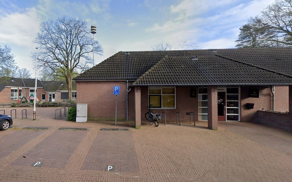 Een entree van een laag gebouw met bakstenen gevel en pannendak. Op de voorgrond parkeerplaatsen.