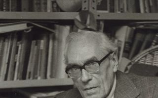 Zwart-witfoto van een oudere man in pak die een opengeslagen partituur in zijn handen houdt.