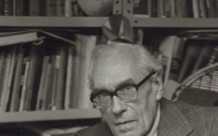 Zwart-witfoto van een oudere man in pak die een opengeslagen partituur in zijn handen houdt.