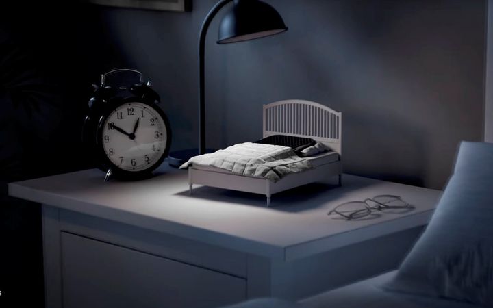 Een miniatuurbedje met een smartphone erop staat op een nachtkastje.