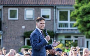 Man staat in de buitenlucht op een podium. Om hem heen staan mensen.