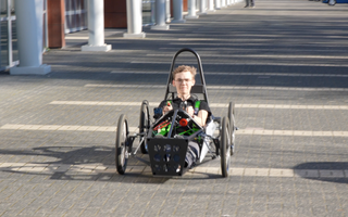 Jongen in zelfgebouwde zwarte elektrische auto die lijkt op een onderstel van een kinderwagen.