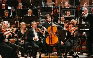 Een jonge cellist treedt op met een orkest. Hij zit als solist vooraan. Alle musici zijn in het zwart gekleed.