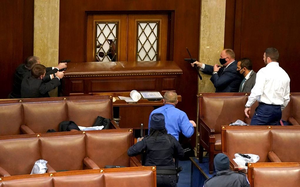 Veiligheidsdiensten van het Capitool met getrokken wapens bij een gemolesteerde deur die toegang geeft tot de vergaderzaal van het Congres. beeld AFP, Drew Angerer