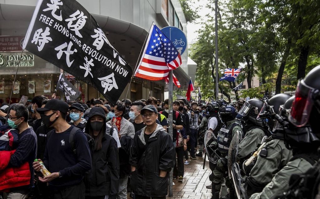 Oproerpolitie kijkt toe hoe demonstranten de straat op gaan in Hongkong, januari 2020. beeld AFP, Isaac Lawrence