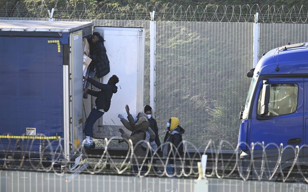 Migranten bestormen een vrachtwagen die in de file staat bij de ingang van de Kanaaltunnel. Ze hopen in het laadruim mee te kunnen liften naar Groot-Brittannië. beeld AFP, Denis Charlet