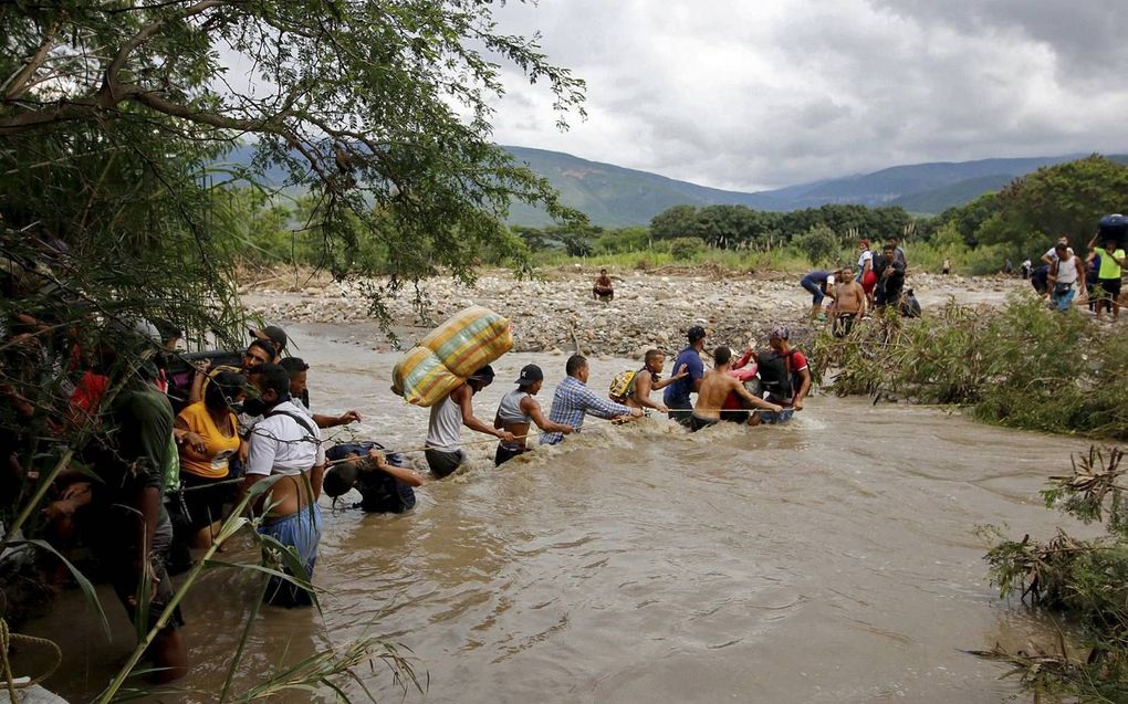 Venezolanen lopen aan de hand van een touw de Tachirarivier over, november 2020. De rivier vormt de  natuurlijke grens tussen Colombia en Venezuela. Colombia heeft besloten honderdduizenden migranten op te nemen. beeld AFP, Schneyder Mendoza