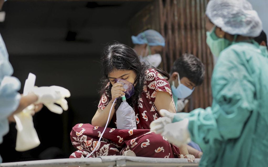 Door een plastic kapje hapt een coronapatiënt in India naar zuurstof. Het is urenlang wachten op opname; alle ziekenhuizen zijn overvol. Voor ziekenhuizen staan rijen ambulances, taxi’s en riksja’s. beeld EPA, Piyal Adhikary