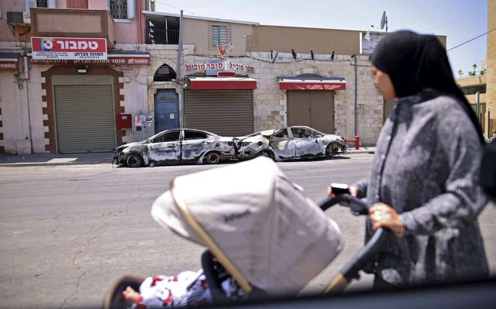 Een Arabisch-Israëlische vrouw loopt langs uitgebrande auto’s in Lod, waar het vorige week tot heftige botsingen tussen Joden en Arabieren kwam. beeld AFP, Ahmad Gharabli