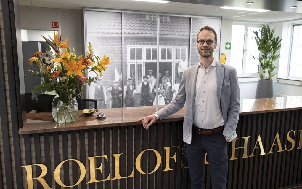 Nico Haase, de vierde directeur van bouwonderneming Roelofs & Haase, bij de receptie van het kantoor in Rijssen. Op de achtergrond een foto van de eerste klus, in 1921.