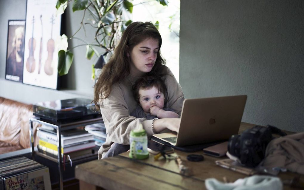 Een thuiswerkende moeder achter haar laptop aan de eettafel met haar kind op schoot. beeld ANP, Richard Brocken