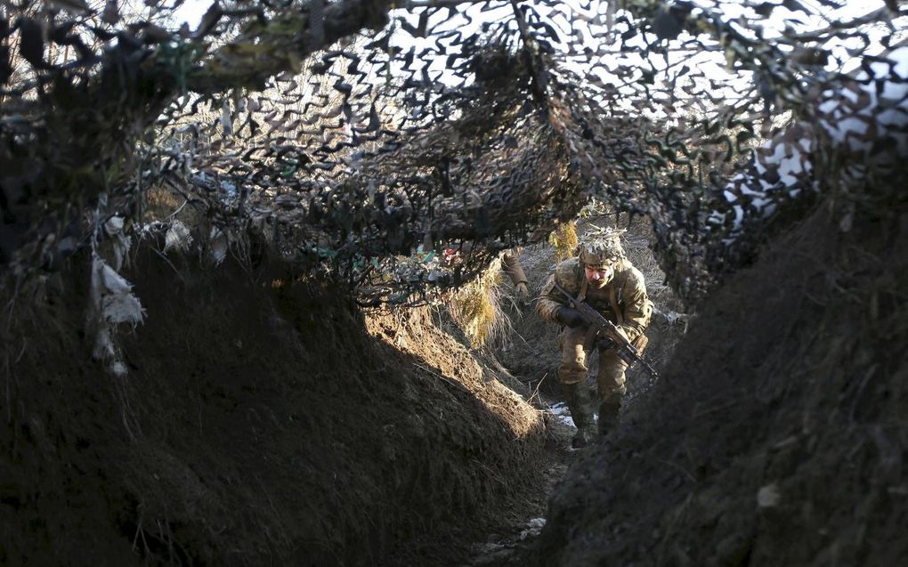 Een Oekraïense soldaat gaat schuil onder een camouflagenet in een loopgraaf langs de grens met door separatisten bezette gebieden in het oosten van Oekraïne. beeld AFP, Anatolii Stepanov