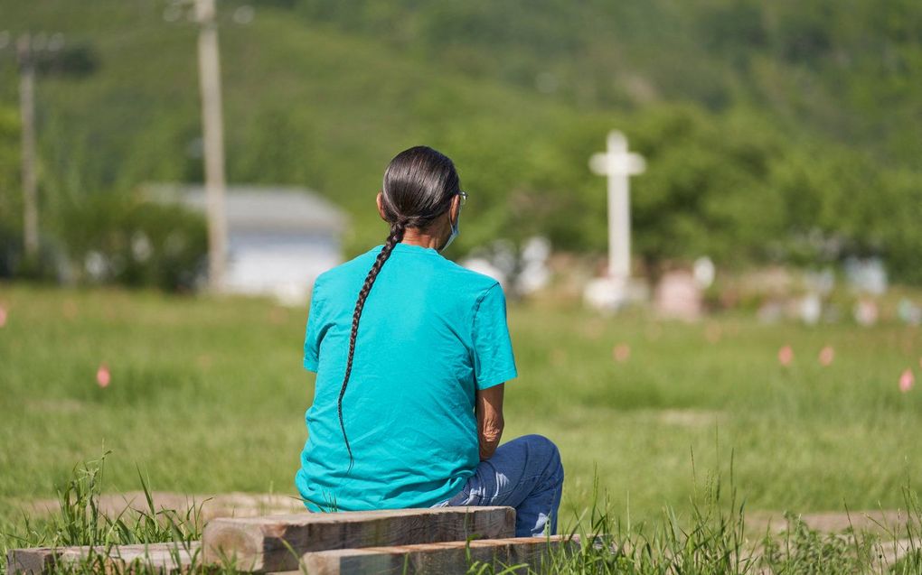 Een man zit op het veld waar de overblijfselen van meer dan 750 kinderen werden begraven op het terrein van de voormalige Marieval Indian Residential School in Cowessess First Nation, Saskatchewan, juni 2021. beeld AFP, Geoff Robins