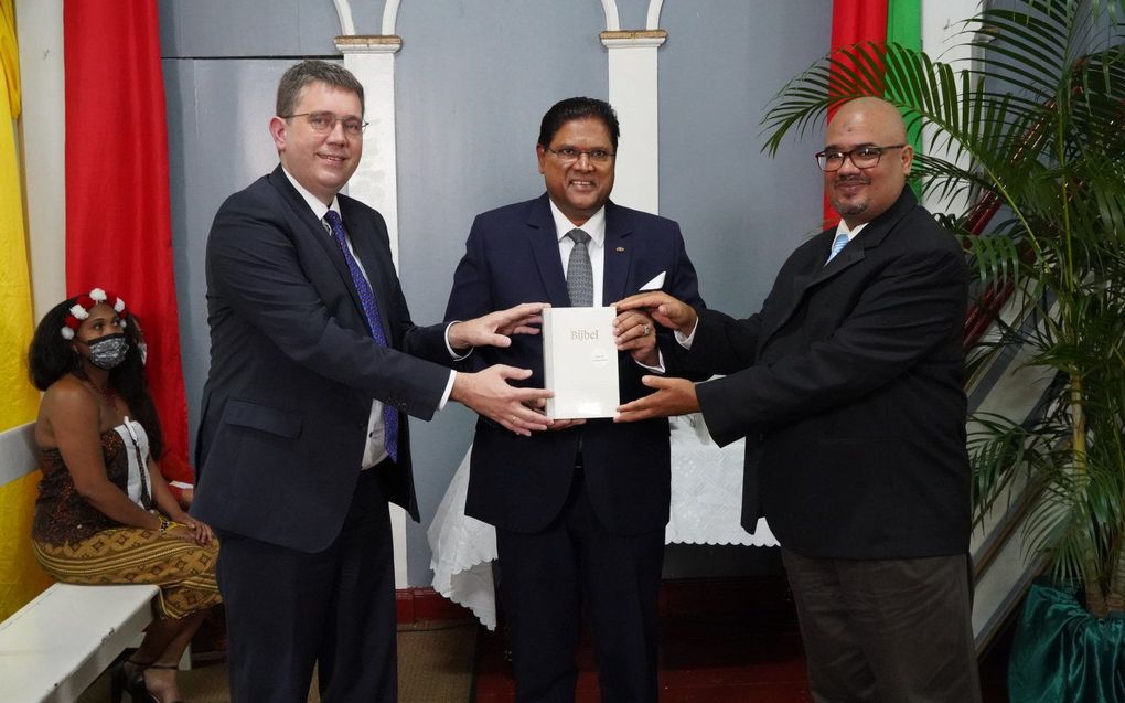 Rieuwerd Buitenwerf (l.) en Erny van Axel (r.) overhandigen de NBV21 aan de Surinaamse president Santokhi. beeld NBG, Paul Doth