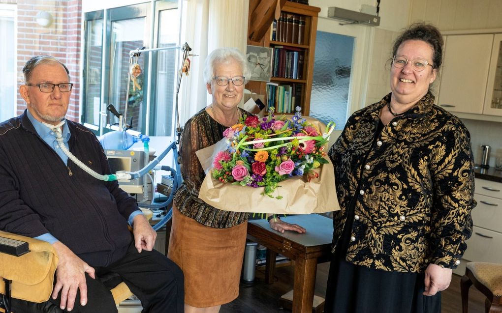 Dochter Anja Grolleman (r.) geeft een bloemetje aan haar moeder Hillie van Laar (m.). Van Laar zorgt trouw voor haar man (l.) die een spierziekte heeft. beeld RD, Anton Dommerholt