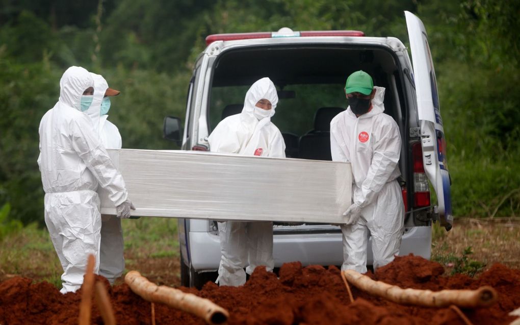 Gekleed in beschermende pakken begraven Indonesische uitvaartmedewerkers een overleden coronapatiënt. beeld EPA, Adi Weda