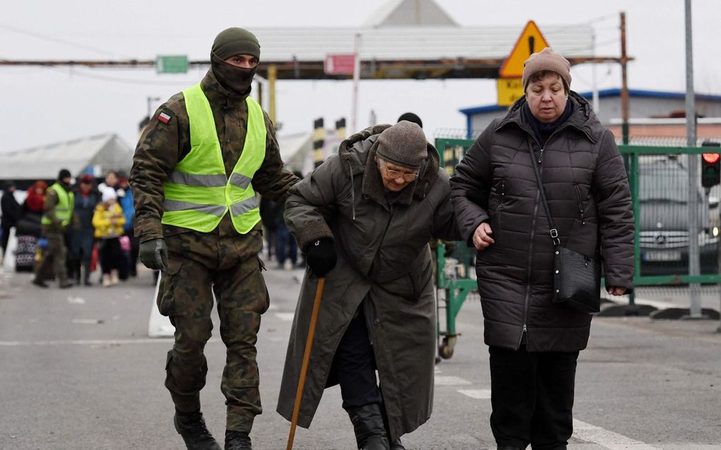 Een Poolse soldaat helpt oudere Oekraïense vluchtelingen bij het Poolse grensdorp Korczowa. beeld AFP, Olivier Douliery