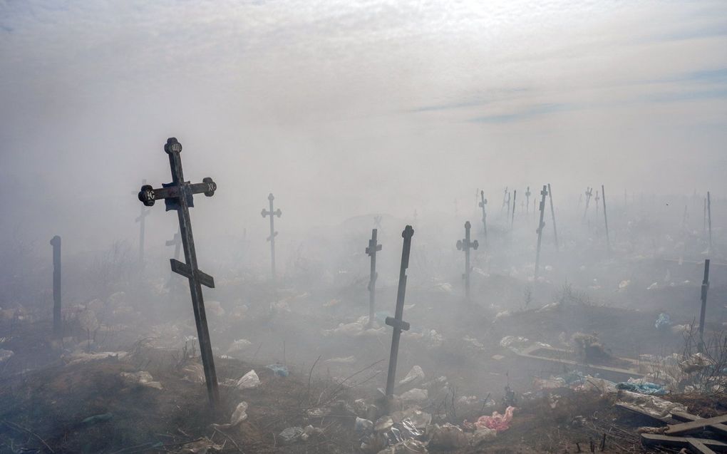 Een kruis steekt boven de vuilnisrook uit op een begraafplaats in Zuid-Oekraïne. beeld AFP, Bulent Kilic