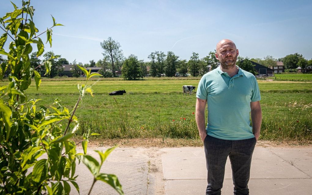 Alex Monster op de begraafplaats waar zowel Johan de Waal als diens broer begraven liggen, met op de achtergrond de boerderij van De Waal. beeld Suzanne Heikoop