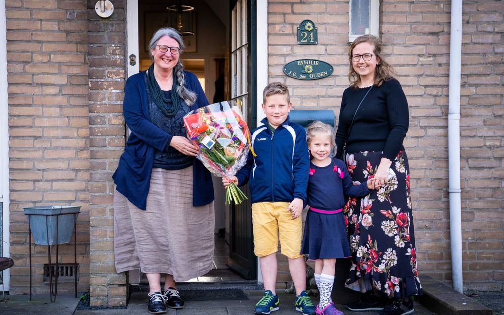 Hanneke Akkerman en haar kinderen Robert en Celine geven een bloemetje aan Judith den Ouden (l.) die met haar man in zelfquarantaine zit. beeld Cees van der Wal