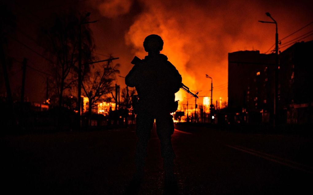 Het silhouet van een Oekraïense militair tekent scherp af tegen een vlammenzee, na een Russische luchtaanval op een gasdepot in Charkiv. beeld AFP, Fadel Senna