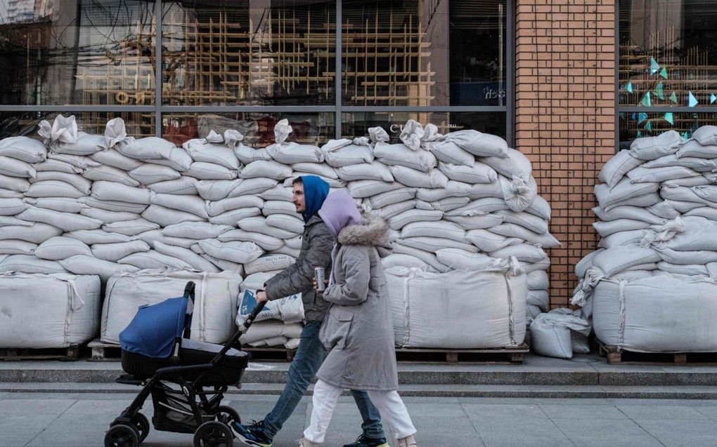 Een jong echtpaar loopt in de Oekraïense stad Dnipro langs een winkel waarvan de ruiten met zandzakken zijn afgeschermd. beeld AFP, Jasujoshi Chiba