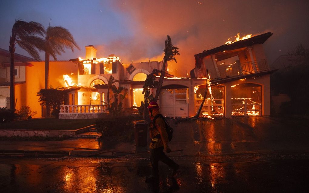 Een brandweerman passeert een woning die in vlammen opgaat, in de Californische plaats Laguna Niguel. Daar vielen deze week zeker twintig huizen ten prooi aan de vlammen. beeld EPA, Etienne Laurent