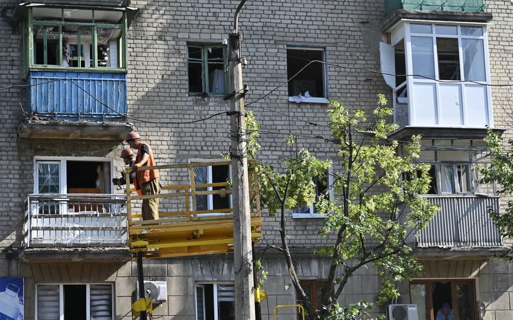 Technici werken voor een beschadigd woongebouw bij een krater van een raketinslag in de Oekraïense stad Bakhmut, Donetsk Oblast. beeld AFP, Genya Savilov