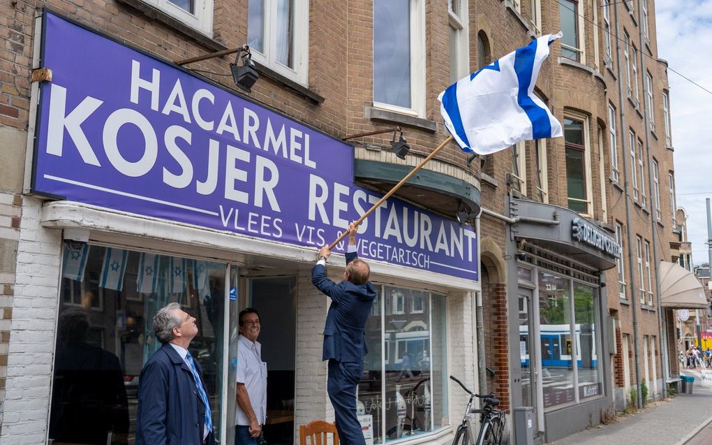 SGP-leider Kees van der Staaij hangt in 2020 de Israëlische vlag uit bij het Joodse restaurant HaCarmel in Amsterdam. beeld SGP
