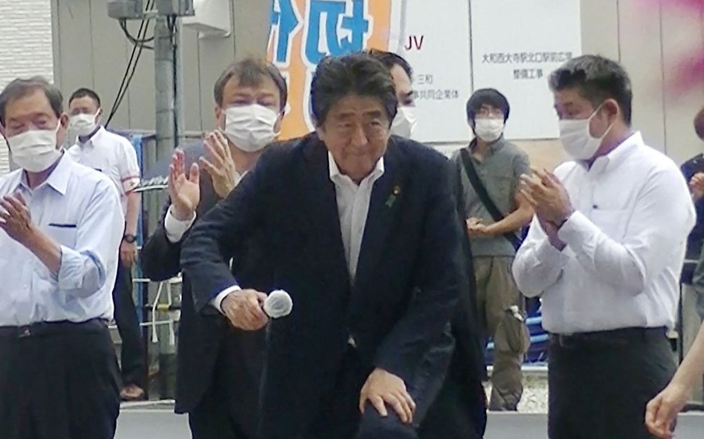 Shinzo Abe (m.) betreedt het podium voor een speech, vlak voordat hij zal worden doodgeschoten. De dader staat rechts van hem op de foto (met groene broek en schoudertas).  beeld AFP, Toshiharu Otani