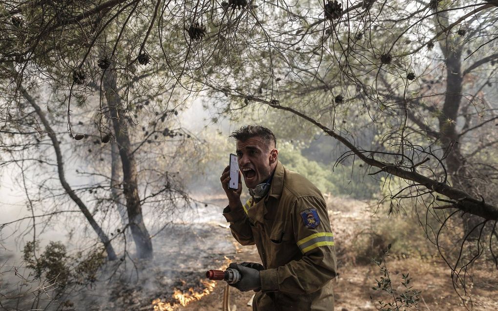 Brandweerman Panagiotis Haratsis, 35, opereert tijdens een bosbrand in de noordoostelijke buitenwijk van Pallini, nabij Athene, Griekenland. beeld EPA, Kostas Tsironis