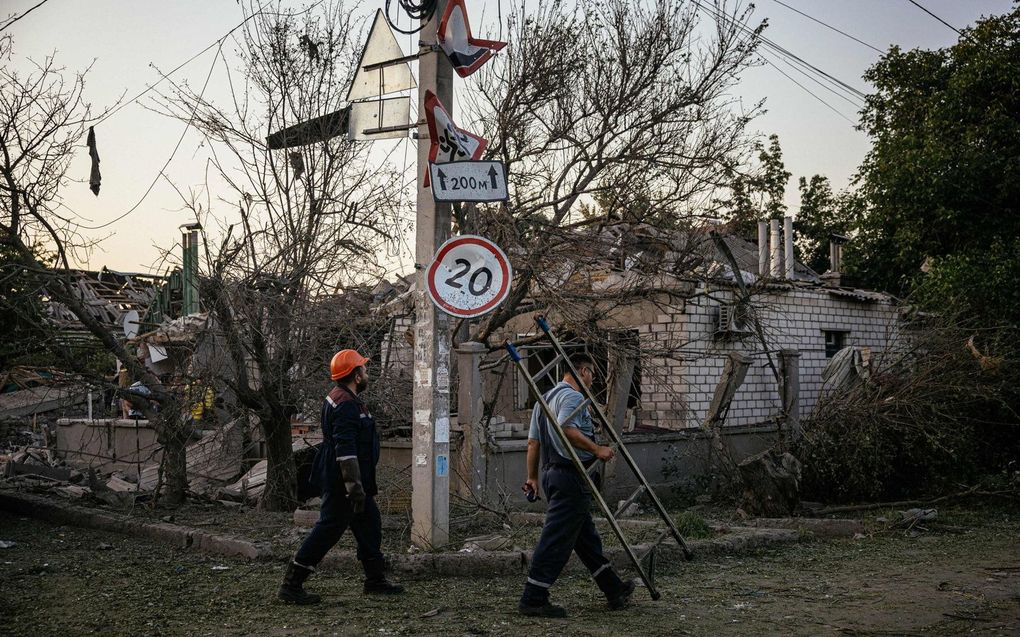 Gemeentewerkers lopen langs verwoeste huizen na een raketaanval in Mikolajiv. beeld AFP, Dimitar DILKOFF