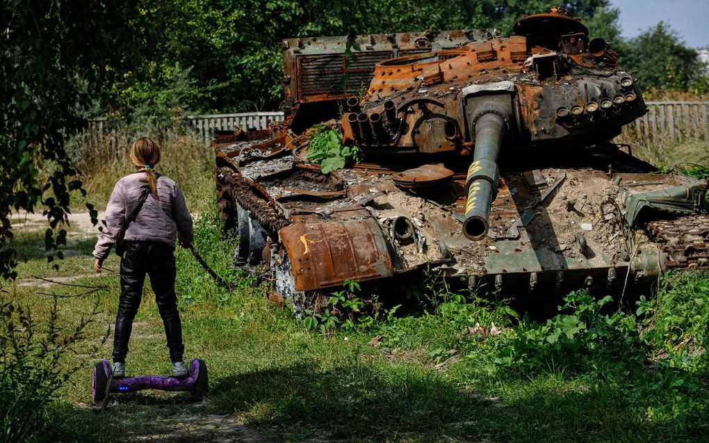 Een meisje op een hoverboard passeert een kapotgeschoten Russische tank in Lukashivka. beeld AFP, Sergei Chuzavkov