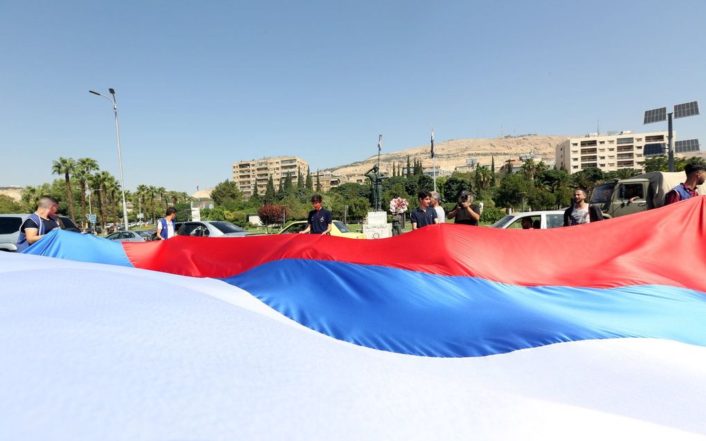 Syriërs zwaaien met een grote Russische vlag tijdens een evenement ter gelegenheid van de Russische Vlaggetjesdag op het Umayyadplein in Damascus, Syrië. beeld EPA, Youssef Badawi