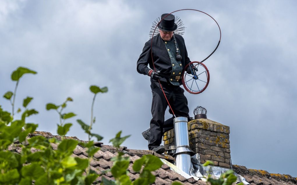 Schoorsteenveger Joop van Leeuwen uit Bodegraven reinigt in een traditioneel schoorsteenvegerspak het rookkanaal van een woning. beeld ANP, Lex van Lieshout