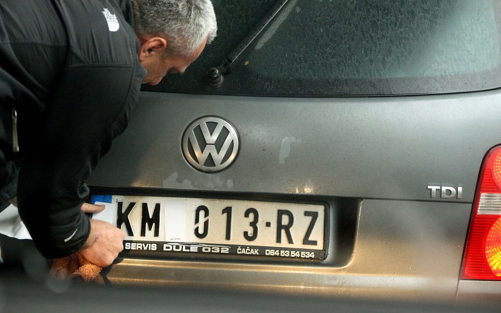 Een automobilist in Noord-Mitrovica verwijdert stickers die de nationale tekens op zijn Servische kentekenplaten bedekken.  beeld EPA/DJORDJE SAVIC