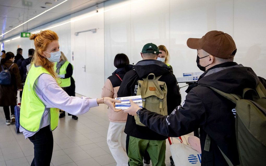 Een medewerker van de GGD deelt op Schiphol gratis coronazelftesten uit onder reizigers uit China.  beeld ANP, Robin van Lonkhuijsen