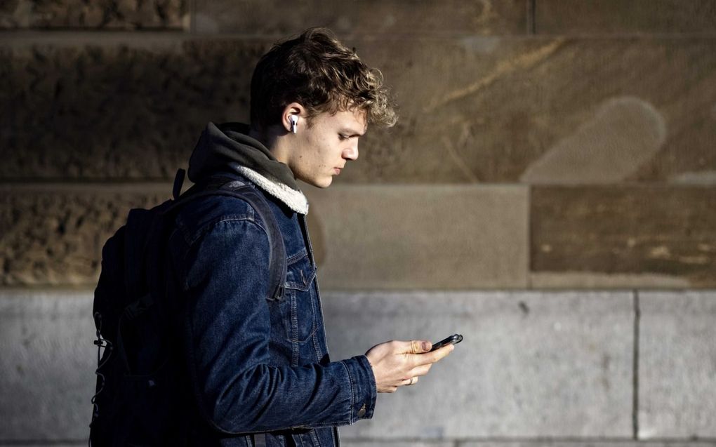 Het mediagebruik van christelijke jongeren verschilt nauwelijks met dat van onchristelijke jongeren. Foto: een jongen kijkt al lopend op zijn smartphone. beeld ANP, Ramon van Flymen.