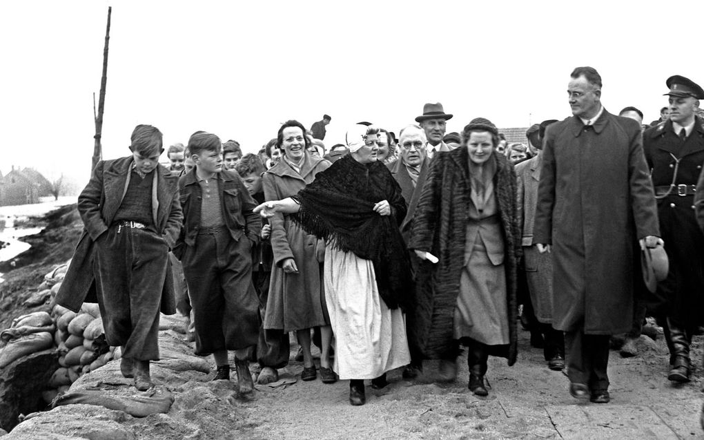 Koningin Juliana tijdens haar bezoek aan het rampgebied bij Kruiningen, laat zich voorlichten door mevrouw Schouwenaar-van Iwaarden in klederdracht. Rechts J. Vader, burgemeester van Krabbendijke. Links Teun Buijzer. Tussen mevrouw Schouwenaar en de koningin staat burgemeester M. Vogelaar van Kruiningen. Achter met hoed staat Jan Blok, dijkgraaf van de Nieuwlandepolder. beeld ANP, G. van der Werff