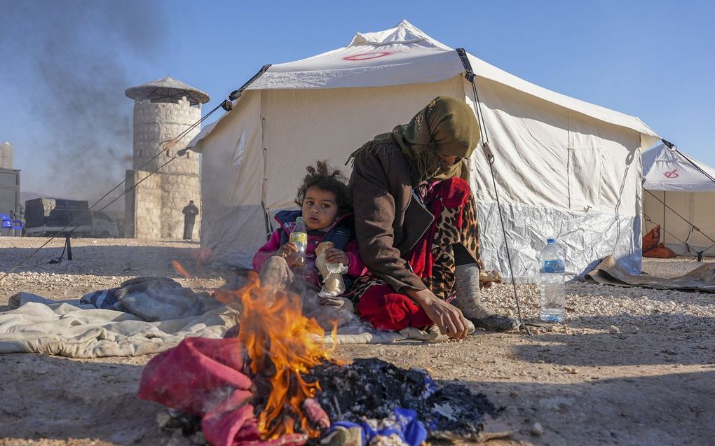 Syriërs warmen zich bij een vuur bij een geïmproviseerd onderkomen voor mensen die dakloos zijn geworden door de aardbeving. beeld AFP, Rami al-Sayed