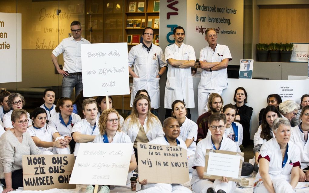 Medewerkers van het Antoni van Leeuwenhoek ziekenhuis zitten op de grond als actie voor een betere cao. De actie is verbonden aan het ultimatum dat de vakbonden hebben gesteld. Die willen dat de Nederlandse Vereniging van Ziekenhuizen tegemoetkomen aan hun eisen om een staking te voorkomen. beeld ANP, Eva Plevier