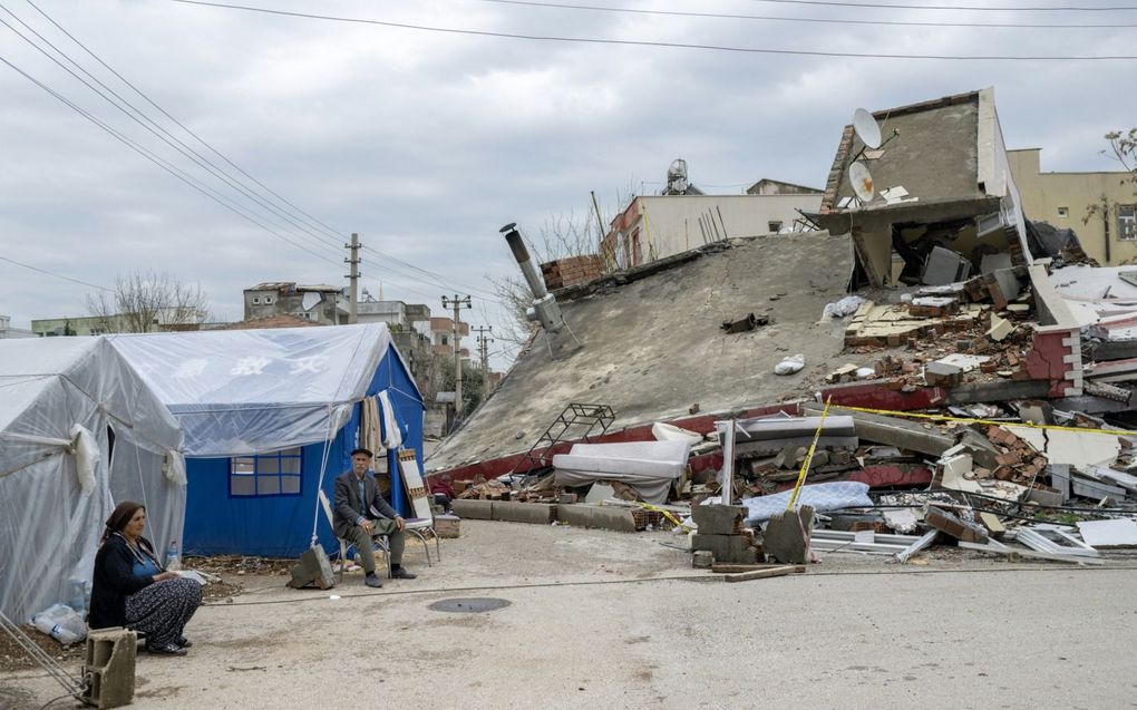 De gevolgen van de aardbeving in Turkije zijn nog volop tastbaar. Abuzer Dede (tweede van links), zit voor zijn tent na zware regenval in Adiyaman in Zuidoost-Turkije. Enkele weken geleden trof een aardbeving met een magnitude van 7,8 de regio. Honderdduizenden Turkse overlevenden zijn ondergebracht in tenten en containerwoningen. beeld AFP, Bulent Kiliç