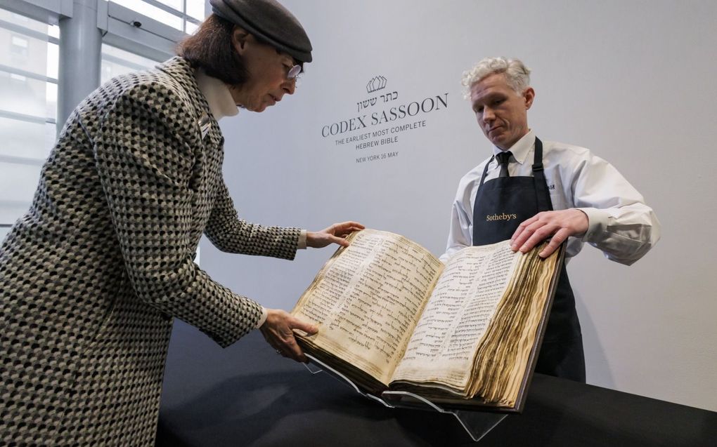 Twee medewerkers van veilinghuis Sotheby’s in New York met in hun handen de Codex Sassoon, het oudste complete manuscript van het Oude Testament. Binnenkort wordt de codex geveild. beeld EPA, Justin Lane