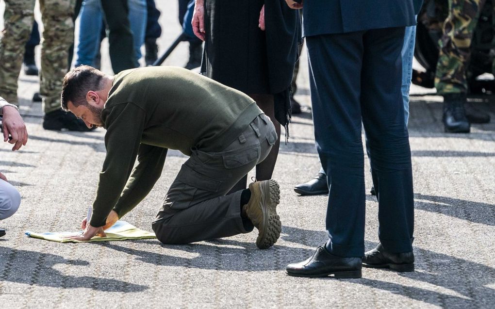 Op de knieën. President Zelensky schrijft op de militaire basis Kamp Soesterberg een boodschap op een vlag. beeld ANP, Jeroen Jumelet