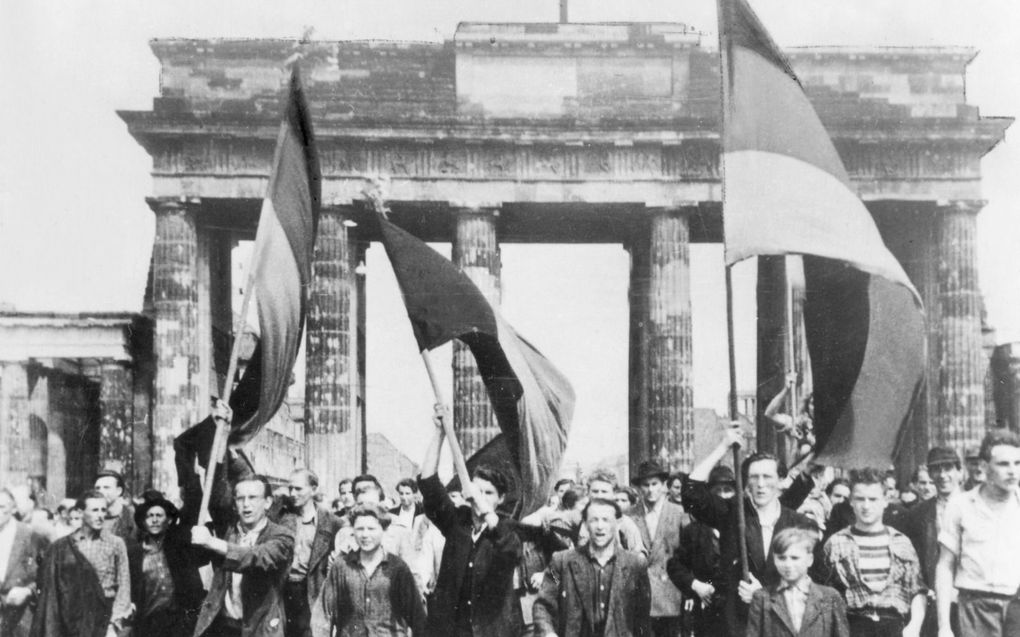 Demonstranten lopen op 17 juni 1953 onder de Brandenburger Tor in Berlijn door. Hun vlaggen zijn versierd met bloemen. beeld Ullstein Bild