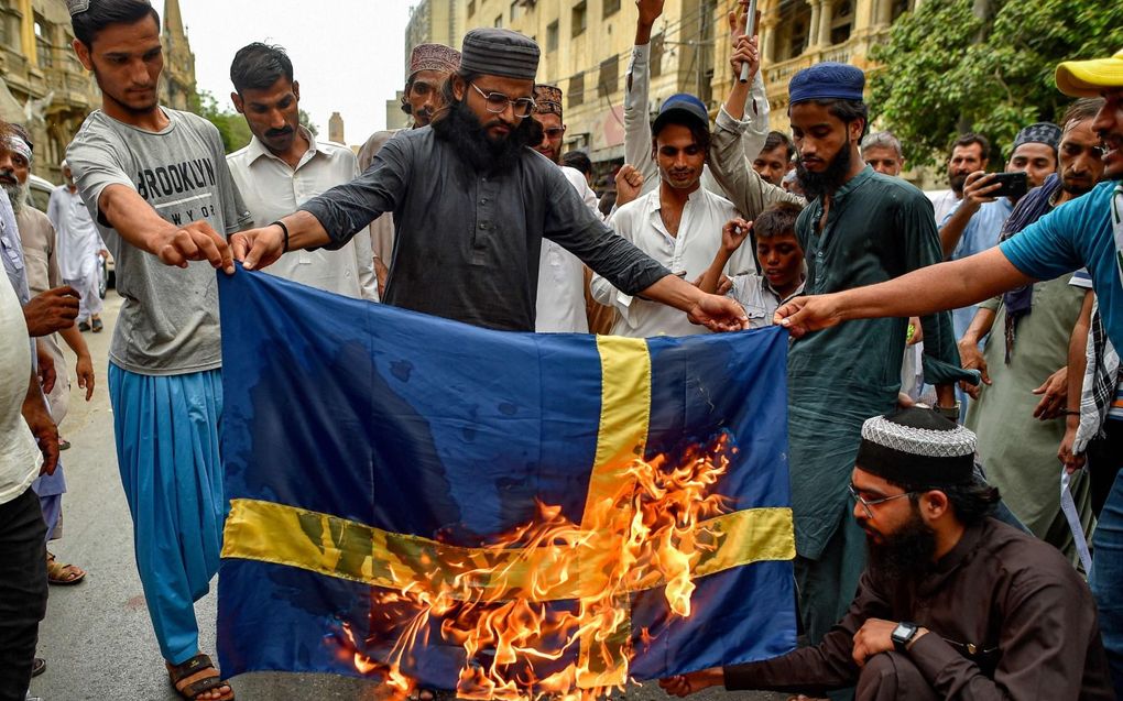 Pakistaanse moslims steken een Zweedse vlag in brand, uit woede om de Koranverbranding in Stockholm. beeld AFP, Asif Hassan