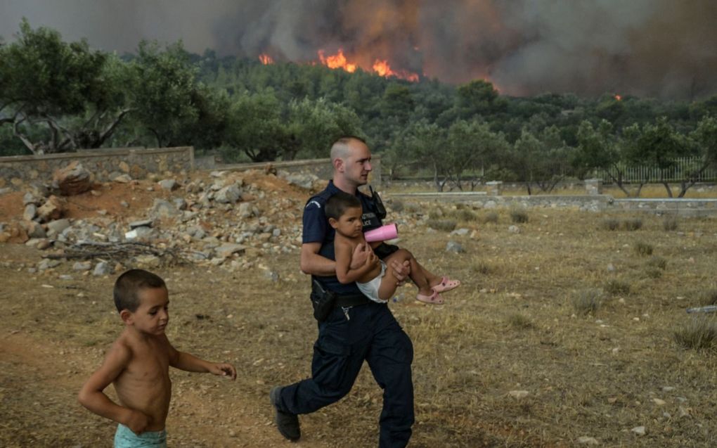 Griekse politieagent evacueert een kind uit een dorp in de buurt van Athene. beeld AFP, Aris Messinis